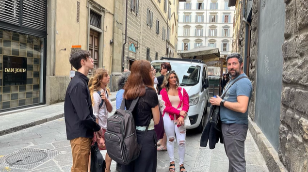 A photo of a group of people standing in a street listening to a person give a presentation.