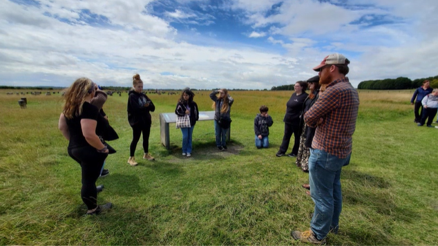 A photo of a group of people standing in a semi circle at woodhenge.