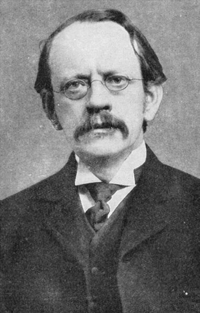 A black and white image of scientist J. J. Thomson wearing a coat and oval shaped spectacles.