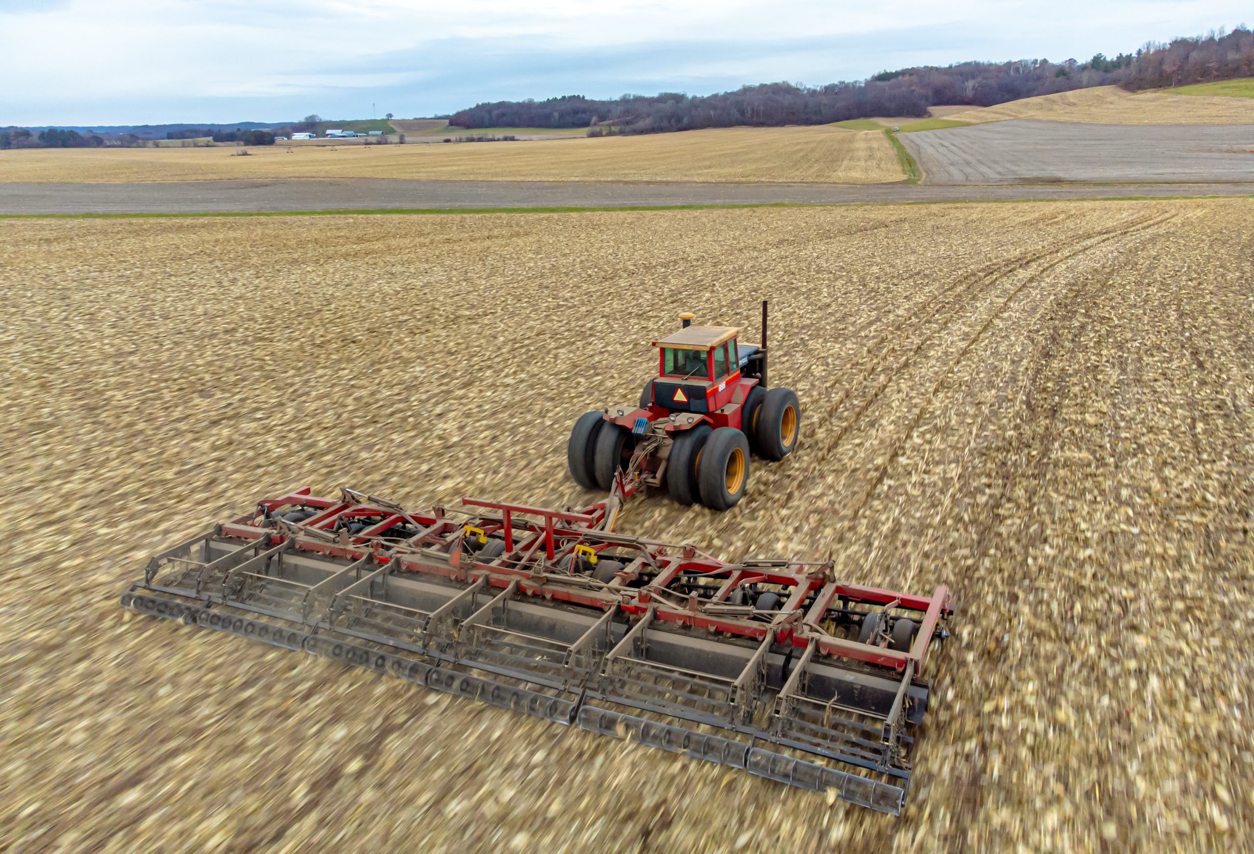 A tractor and tilling tool moving across a corn field after harvest.