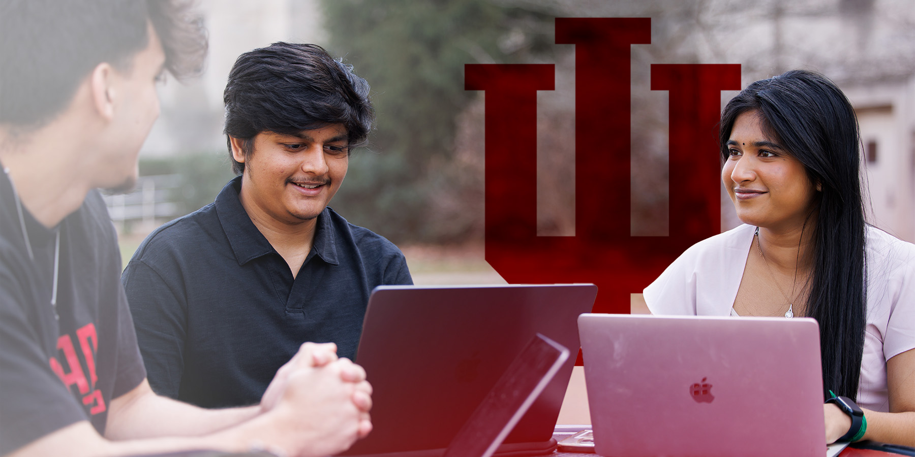 Three students sitting together with their laptops open.