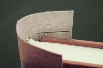Positioning the new spine cloth around the text block spine and marking the turn in