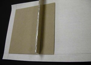 Gluing the binder's board pieces to the cloth using a spacer to position the spine piece