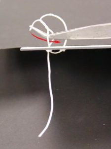 Pulling the loose end of the tie around the edge of the board and through