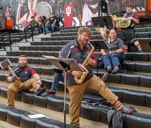 Men and women holding musical band instruments on gym bleachers.