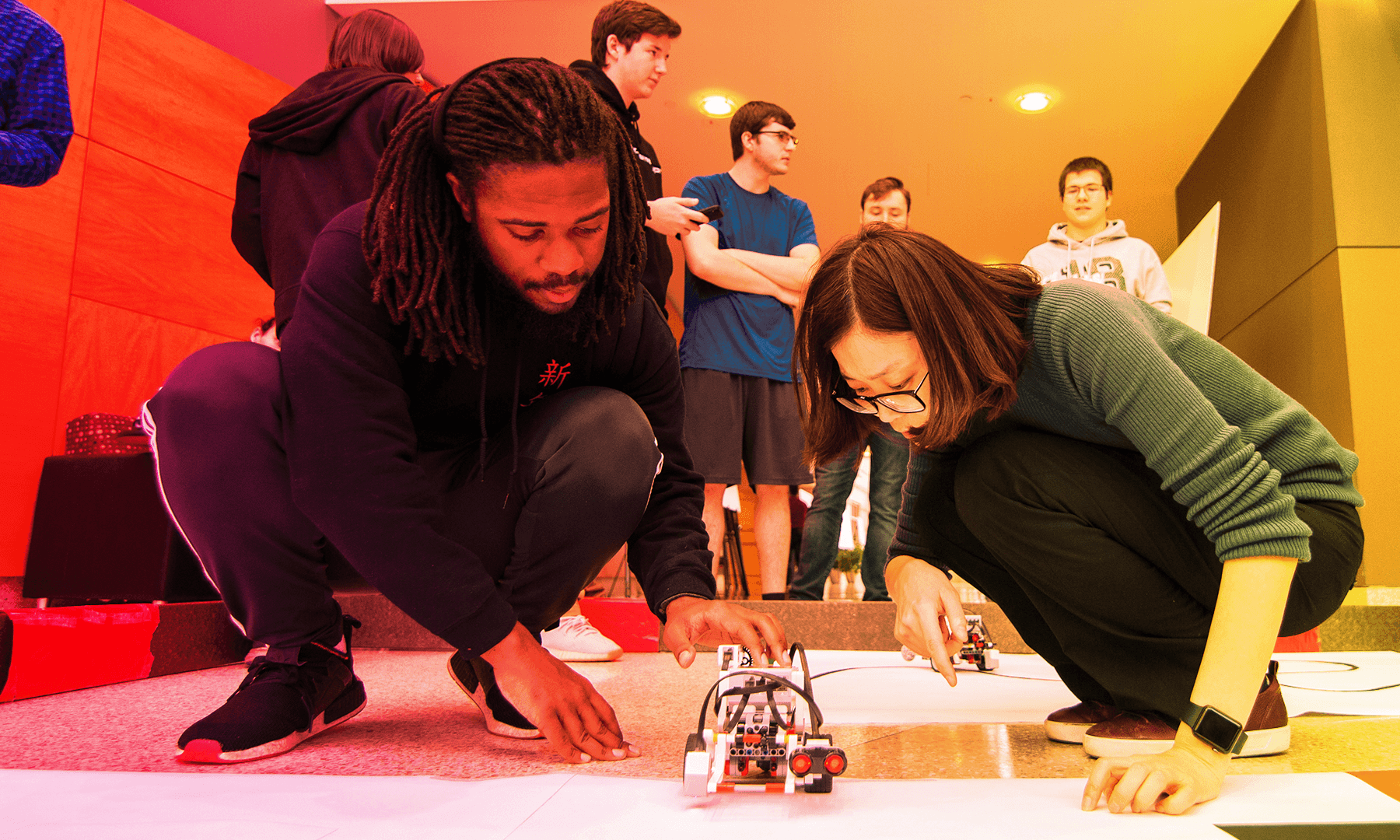African American male and Asian female crouched down working with a robot