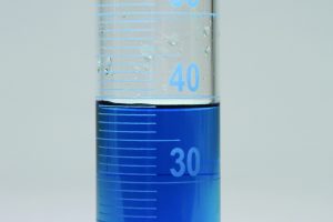 A graduated cylinder with blue water in it showing a meniscus between the 37 and 38 mL graduations with the bottom of the meniscus slightly closer to the 38 mL graduation than the 37 mL graduation.