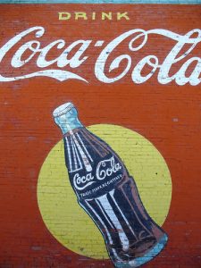 A Coca-Cola advertisement painted on a brick wall. The advertisement includes the Coca-Cola logo and an image of a Coke bottle.