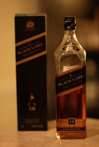 A bottle of Johnnie Walker Black Label whiskey standing next to its box on a countertop.