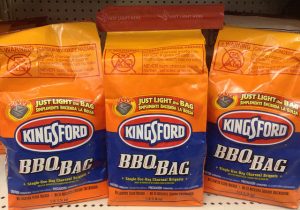 Three bags of Kingsford brand grilling charcoal sitting on a store shelf.
