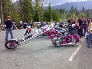 A crowd of people standing and looking at customized motorcycles in a parking lot.