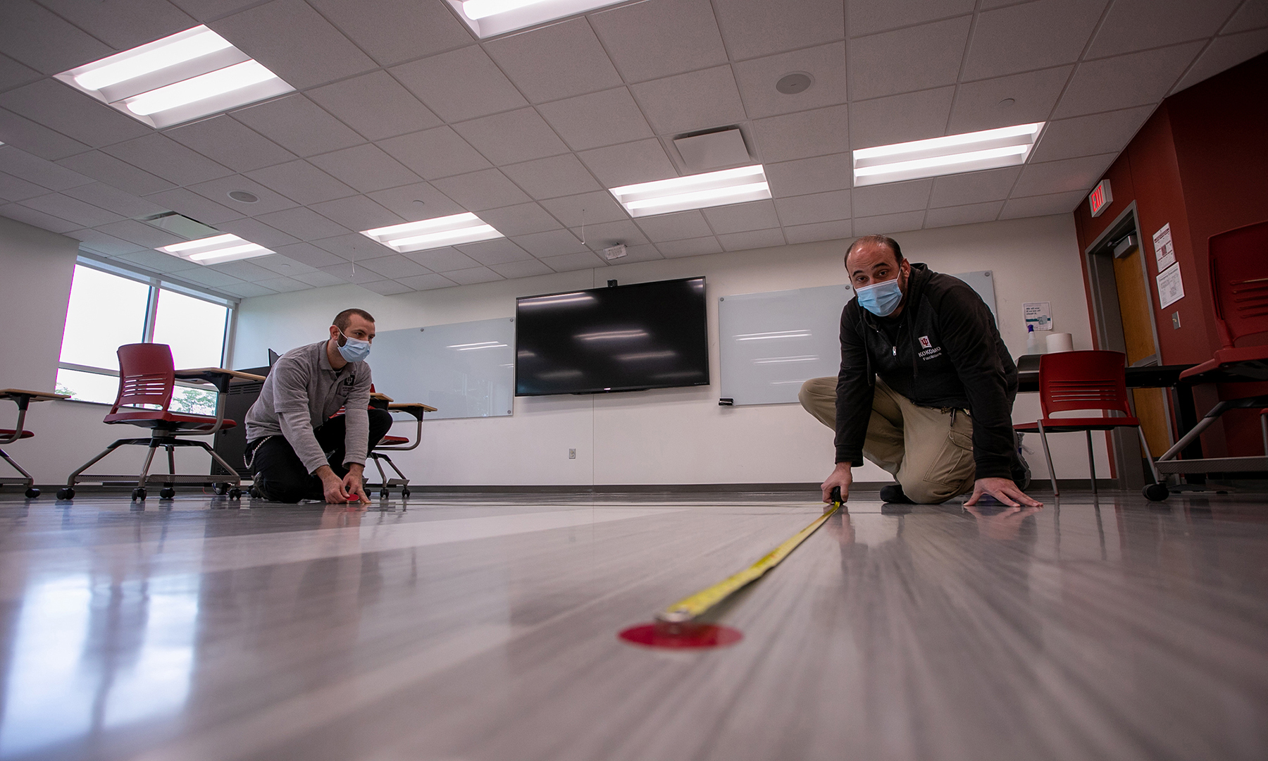 two male workers measuring the floor with tape measures