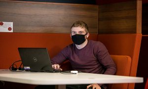 male student on laptop in library wearing mask