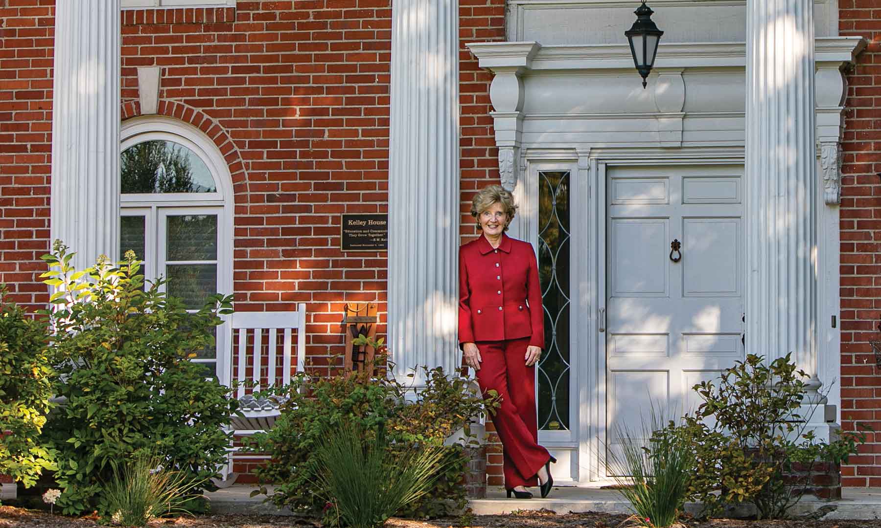 Chancellor Susan Sciame-Giesecke in a red pant suit in front of a brick home with white columns