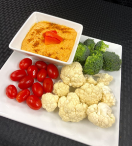 red pepper hummus with tomato, cauliflower, and broccoli on a plate